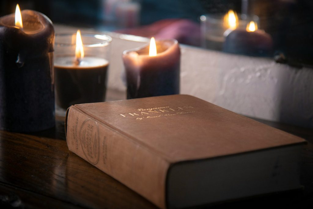 brown hardbound book near lighted pillar candles
